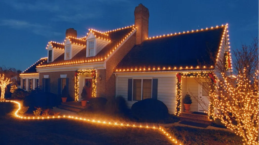 A brick cape home in warm white lights with a lit walkway