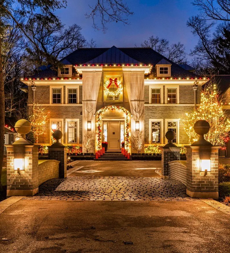 A lit facade and driveway pillars on a brick colonial