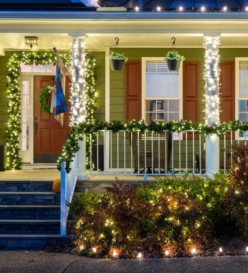 Garland and lit shrubs across a covered porch