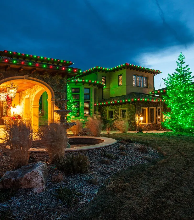 A stucco home in permanent red and green beside a green-lit conifer